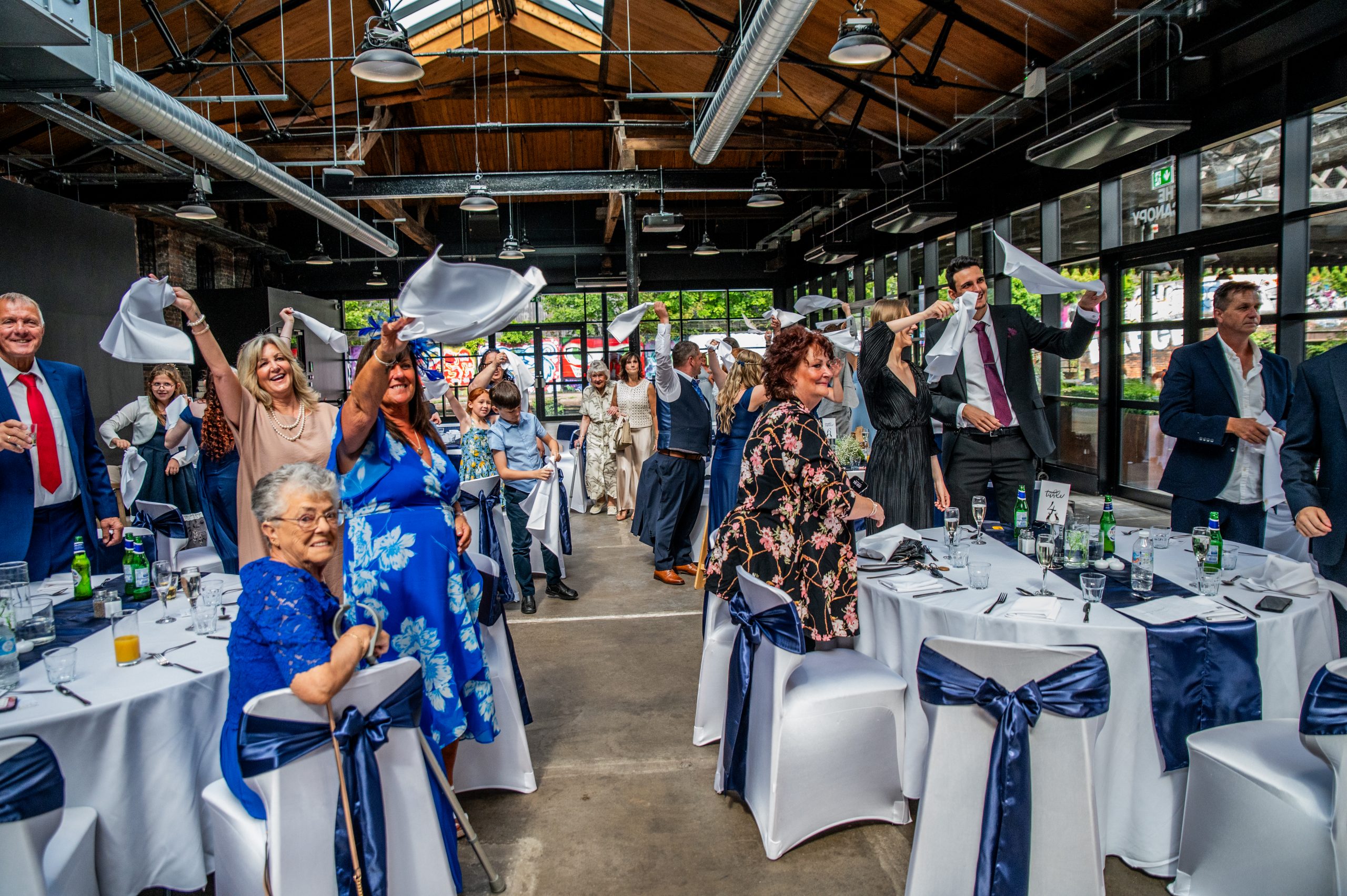 The bond set up for a wedding reception with chair covers and navy sashes and people celebrating