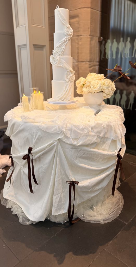 wedding cake, cake table draping and candles and fresh floral display